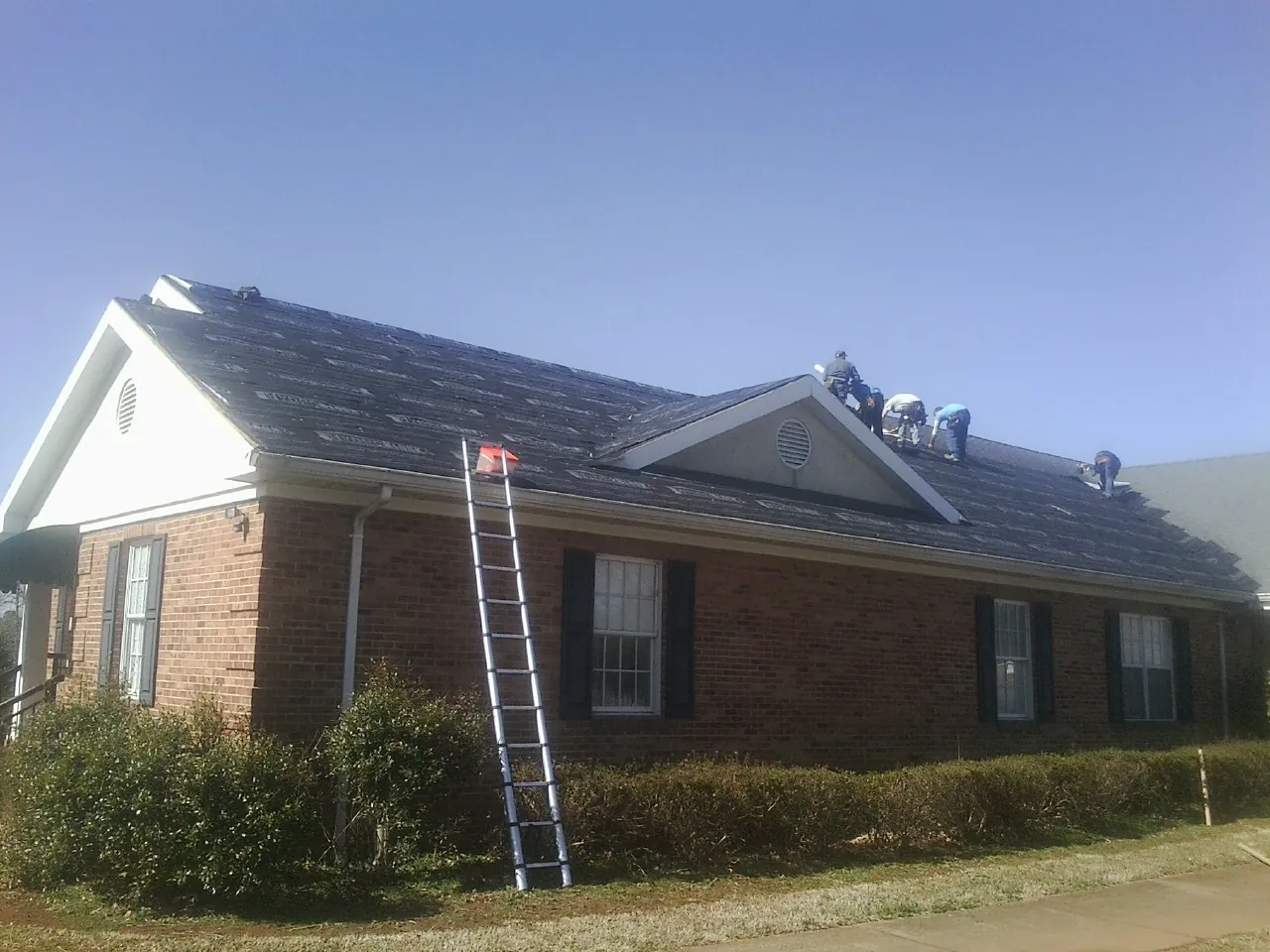 Crew tearing shingles off a brick ranch roof with a ladder set — Metal Roof Repair work by our crew in Mifflin