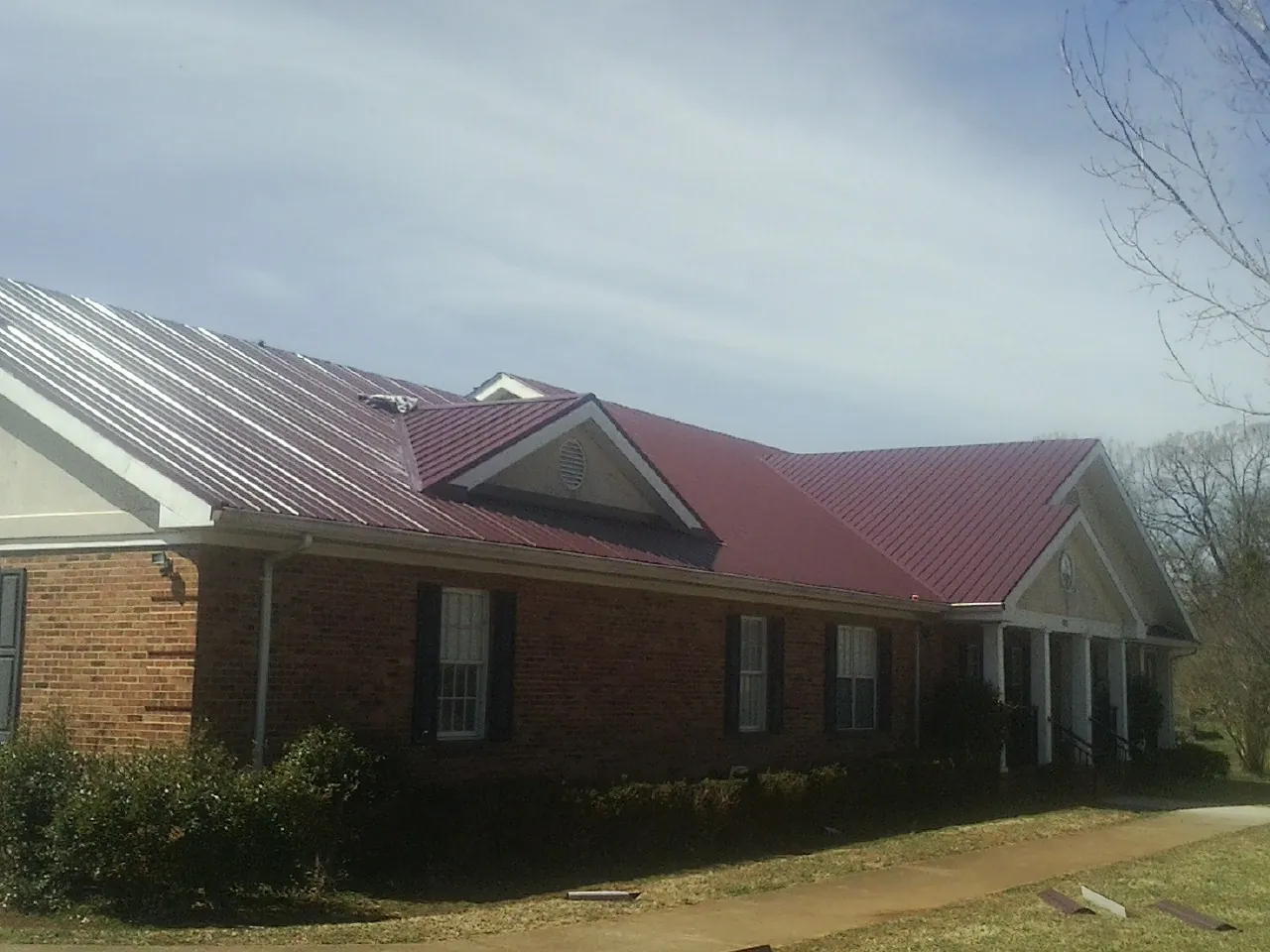 Red metal roof with gabled entries on a long brick building, from a Hail Damage Roof Repair job in Mifflin