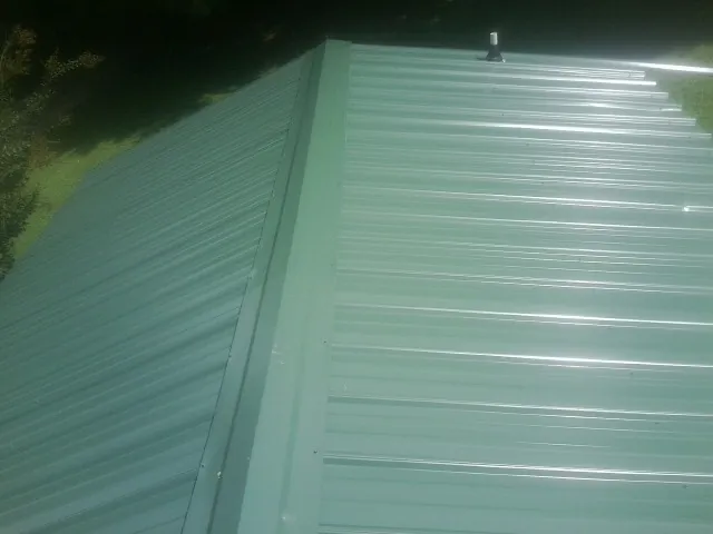 New green metal panels meeting at the ridge of a roof — Flat Roof Repair work by our crew in Mifflin