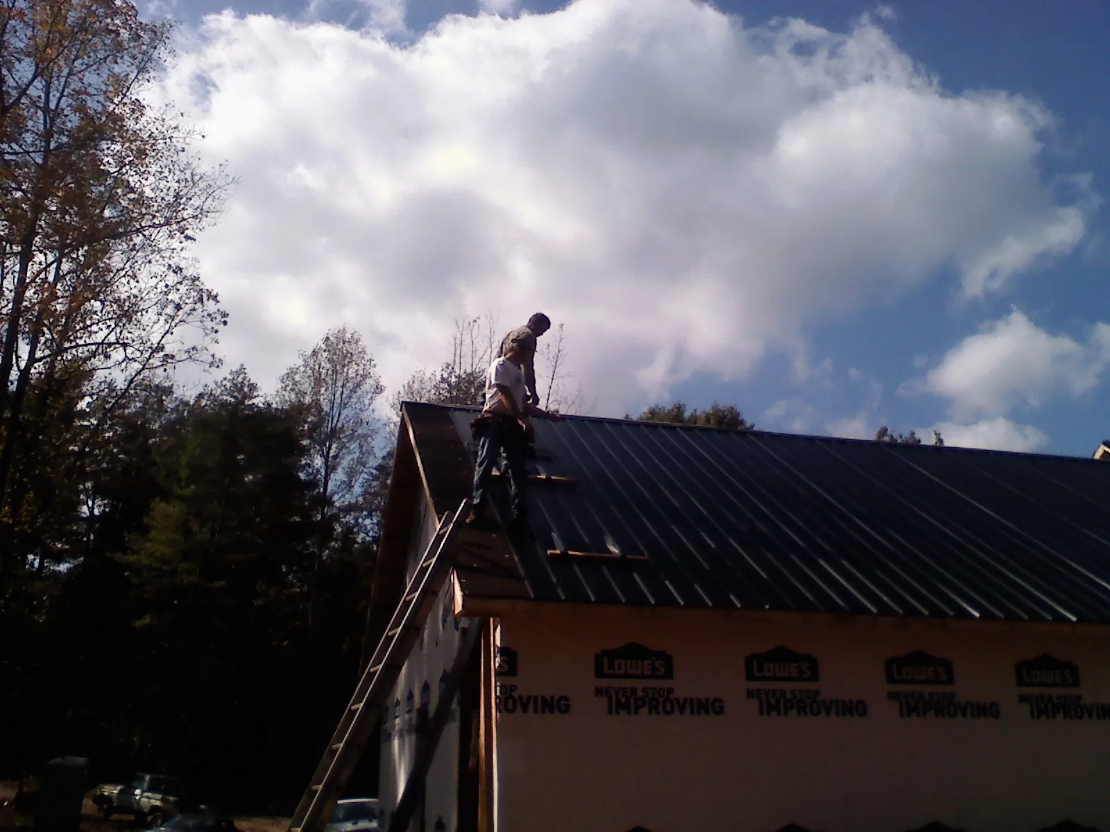 Roofer fastening dark metal panels high against a cloudy sky, from a Roof Inspection job in Mifflin